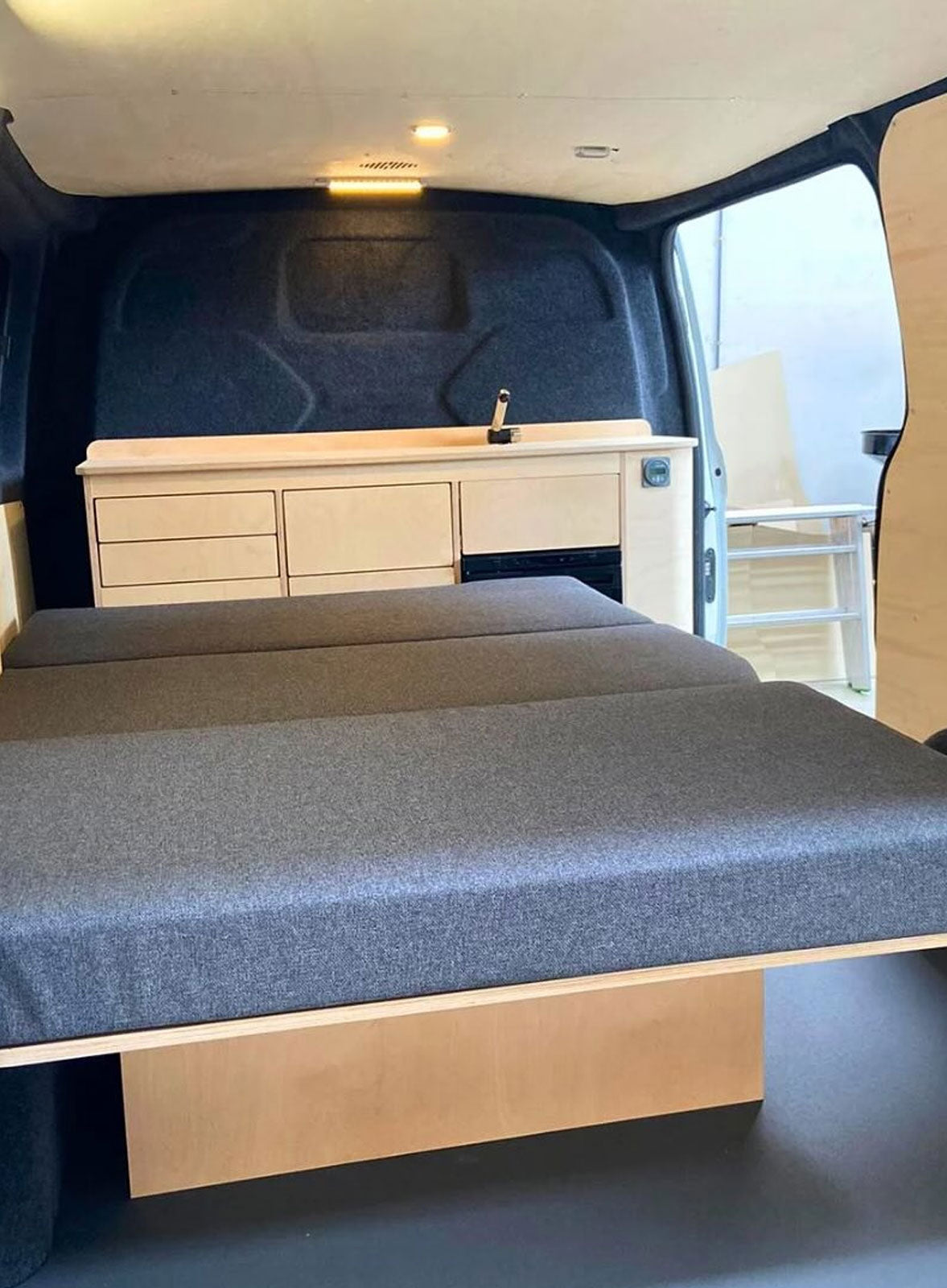 Banquette clic-clac classique 120 cm Exokit en finition soupçon de blanc avec coussins tissu gris dans un Ford Transit Custom L1H1 aménagé par Roadstore