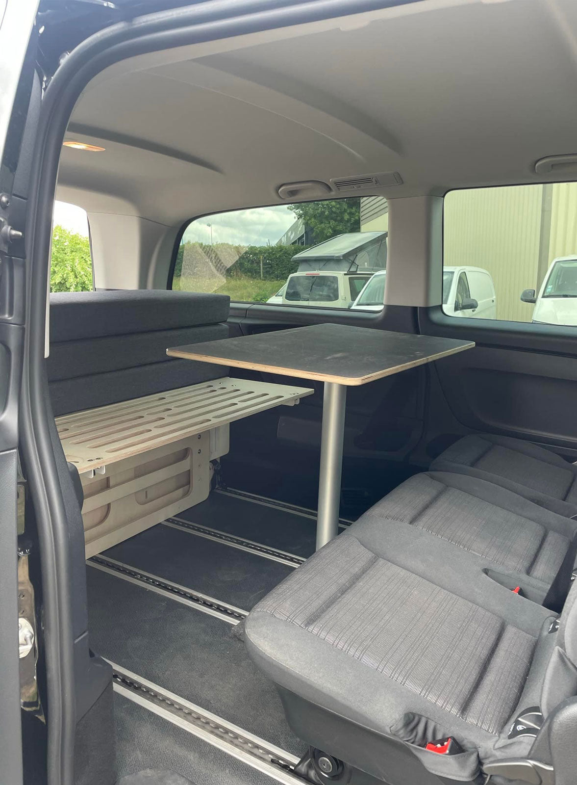 Configuration salon repas dans un Mercedes Vito Tourer avec sièges tournés dos à la route, table centrale et Minimalle Exokit à l'arrière